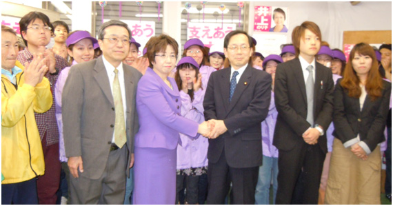 井上のりこ市議とがっちり握手し、勝利を祝う竹内代表=10日 井上のりこ市議とがっちり握手し、勝利を祝う竹内代表=10日